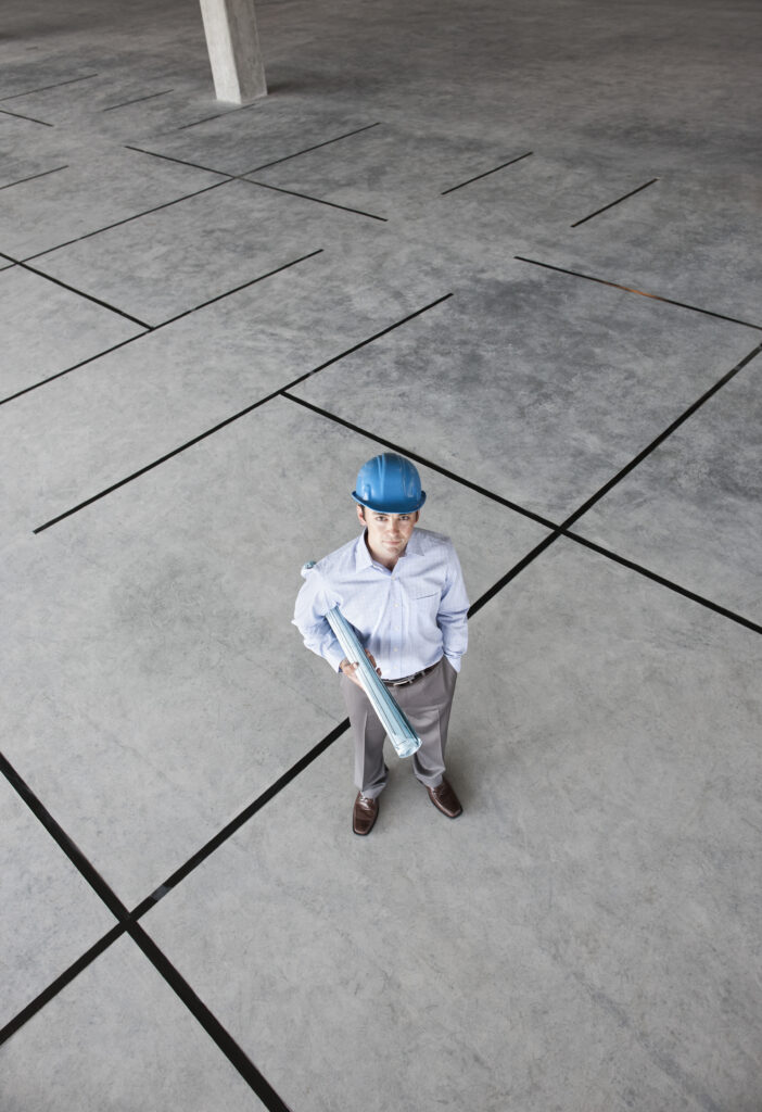 Caucasian businessman holding plans for a new office in a large empty raw office space.